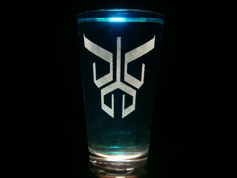 May include: A clear glass shot glass with a blue liquid inside. The glass has a white, geometric design etched into the side.