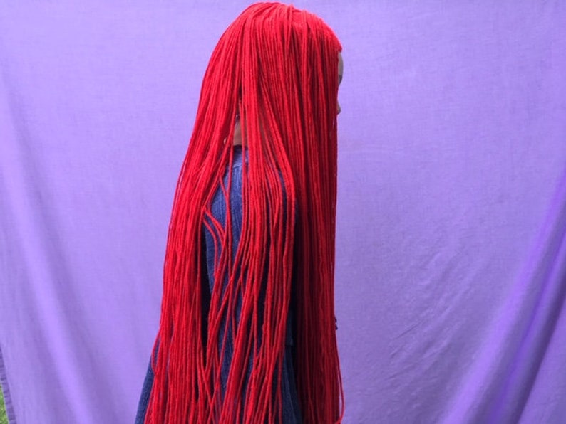 May include: A person is seen from the side, their face obscured by long, vibrant red strands of hair. The hair cascades down, contrasting with a denim jacket. The background is a solid, soft purple.