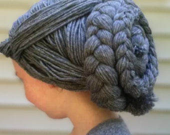May include: A gray knitted hat with a braided design. The hat is made of thick yarn and has a textured appearance. The braid is positioned on the side of the head, adding a unique style to the headwear.