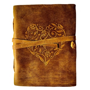 May include: A brown leather journal with a decorative heart design embossed on the front cover. The journal has a leather strap closure.
