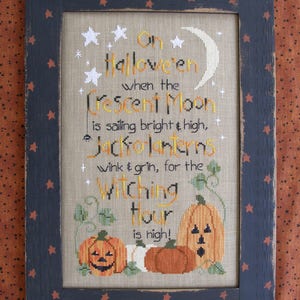 Può includere: Un ricamo a punto croce incorniciato con una cornice nera e uno sfondo beige. Il disegno presenta una luna crescente, stelle e il testo "On Halloween when the Crescent Moon is sailing bright & high, Jack-o-Lanterns wink & grin, for the Witching Hour is high!"