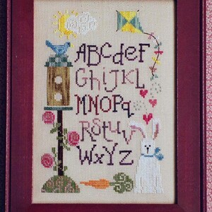 May include: A cross-stitch embroidery featuring the alphabet, a birdhouse, a bunny, a kite, a carrot, and flowers. The letters are in a vintage style font.