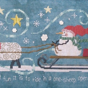 May include: A cross-stitch pattern of a snowman riding a sled pulled by a sheep. The scene is set against a blue background with white snowflakes and yellow stars. The text "Oh, what fun it is to ride in a one-sheep open sleigh!" is at the bottom of the image.