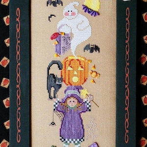 Może przedstawiać: Haftowany krzyżykiem obraz przedstawiający czarownicę z dynią, duchem i czarnym kotem. Czarownica trzyma różdżkę i ma na sobie fioletową sukienkę. Haftowany obraz jest oprawiony w czarną i czerwoną ramę, z wiszącą u dołu torbą "Trick or Treat".