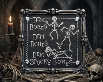 May include: A square cross-stitch embroidery on black fabric featuring white skeletons and the text "DEM BONES DEM BONES DEM BONES SPOOKY BONES". The piece is encased in a dark, metallic frame molded to resemble interconnected human bones.