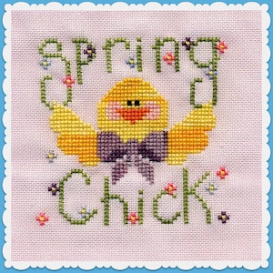 May include: Cross-stitch design featuring a yellow chick with a purple bow tie, the words "SPRING CHICK" in green, and small floral accents. The design is on a light pink fabric with a scalloped blue border.