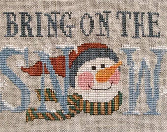 May include: Cross-stitch pattern featuring a snowman with a blue hat and scarf, and the text "Bring on the Snow!"