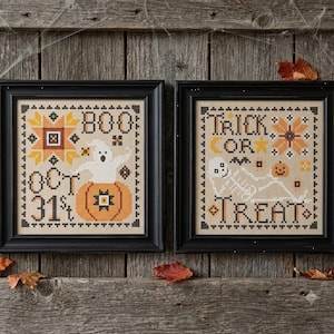 May include: Two framed cross-stitch patterns on beige fabric. The left piece features a ghost in a pumpkin with the text BOO and OCT 31. The right piece shows a skeleton with a pumpkin and the text TRICK OR TREAT. Both are in black frames.