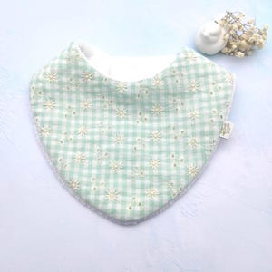 Peut inclure: Bavoir pour bébé à carreaux vert menthe et blanc, orné de motifs floraux brodés. Le bavoir a un envers blanc doux et une forme arrondie. Une petite étiquette est attachée sur le côté.