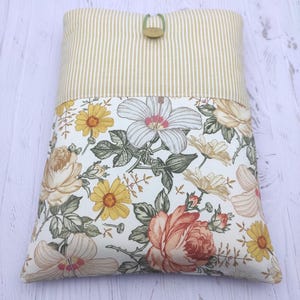 Può includere: Una custodia rettangolare in tessuto con un motivo floreale e una parte superiore a righe. Il motivo floreale presenta grandi rose, margherite e fiori di ibisco nei toni del pesca, giallo e bianco. La parte superiore è beige chiaro con strisce verticali e ha una chiusura a bottone.