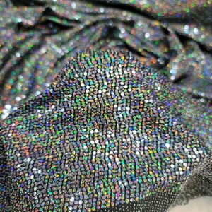 May include: Close-up of iridescent fabric with a textured, sparkly surface. The fabric is black with small, round, multi-colored sequins.