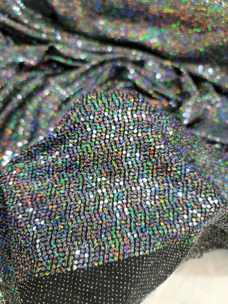 May include: Close-up of iridescent fabric with a textured, sparkly surface. The fabric is black with small, round, multi-colored sequins.