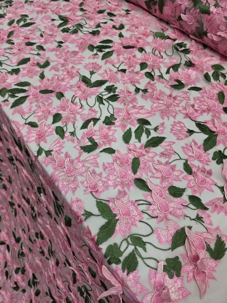 Puede incluir: Tela de encaje bordado floral rosa con hojas verdes. El delicado dise&ntilde;o presenta flores y enredaderas tridimensionales, creando un aspecto texturizado y elegante. Ideal para vestidos, faldas u otras prendas.