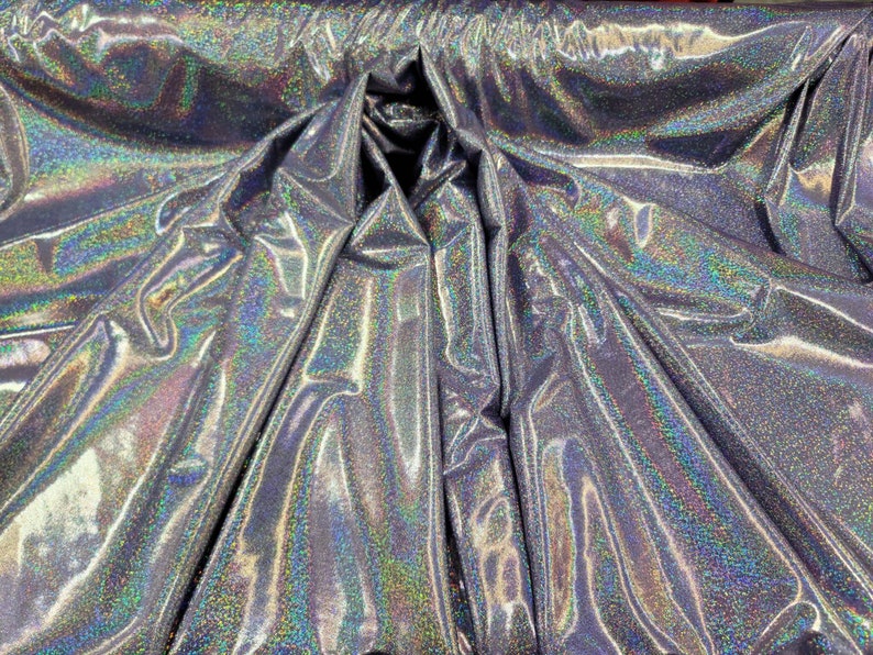May include: Silver iridescent fabric with a glittery finish. The fabric is folded and draped, showing its texture and sheen.