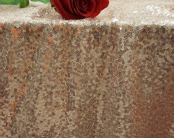 May include: A single red rose lying on a rose gold sequin tablecloth.
