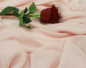 May include: A single red rose with green leaves lies on a soft, pale pink fabric.