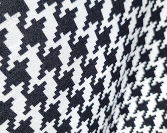 May include: Close-up of a fabric with a black and white houndstooth pattern. The pattern is a repeating design of abstract shapes, creating a textured appearance. The fabric is slightly wrinkled, suggesting it is a soft material.
