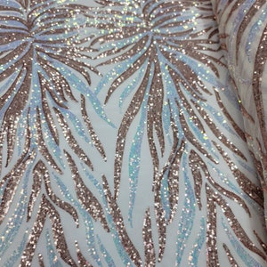 May include: A close-up of iridescent blue and rose gold sequins on a white mesh fabric. The sequins are arranged in a pattern of curved lines.