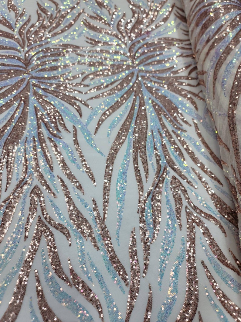 May include: A close-up of iridescent blue and rose gold sequins on a white mesh fabric. The sequins are arranged in a pattern of curved lines.
