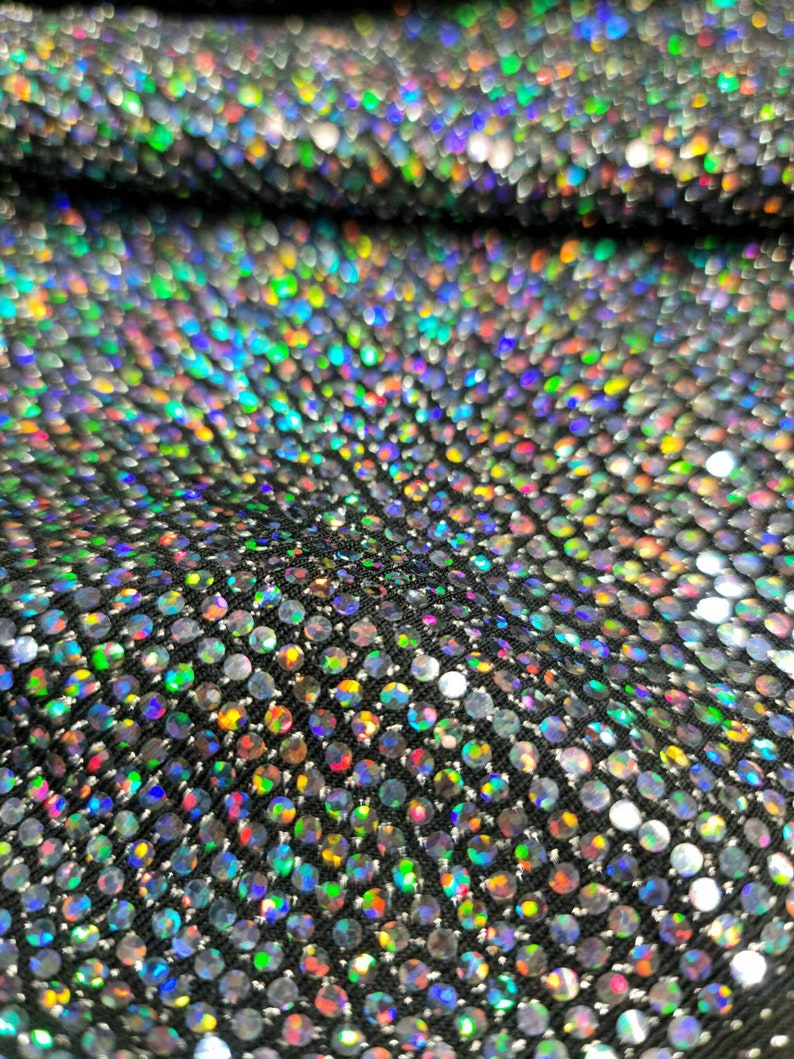 May include: Close-up of iridescent fabric with a pattern of small, round sequins. The sequins are arranged in a repeating pattern and create a shimmering effect.