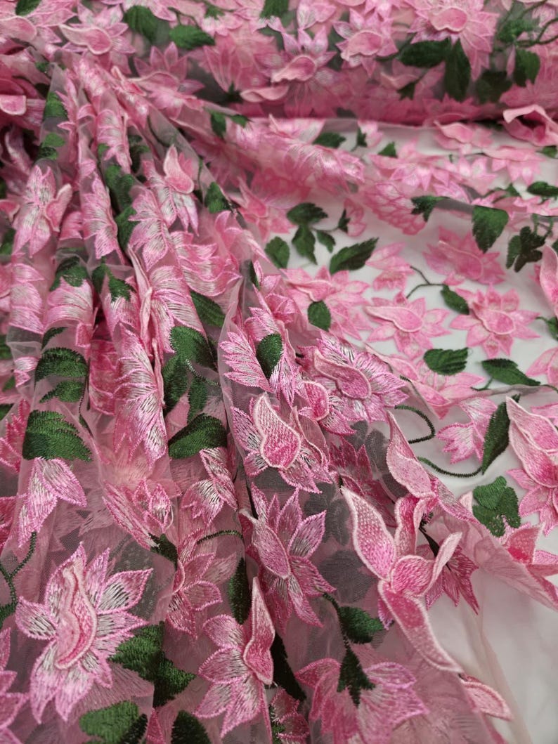 Puede incluir: Primer plano de tela bordada con flores rosas. La tela presenta flores rosas detalladas en tres dimensiones con hojas verdes, creando un efecto texturizado y en capas. El fondo transparente a&ntilde;ade profundidad al dise&ntilde;o. Ideal para prendas y proyectos de artesan&iacute;a.