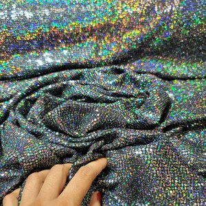 May include: Close-up of iridescent black fabric with a textured, sparkly finish. The fabric is folded and draped, showing its shimmery quality.
