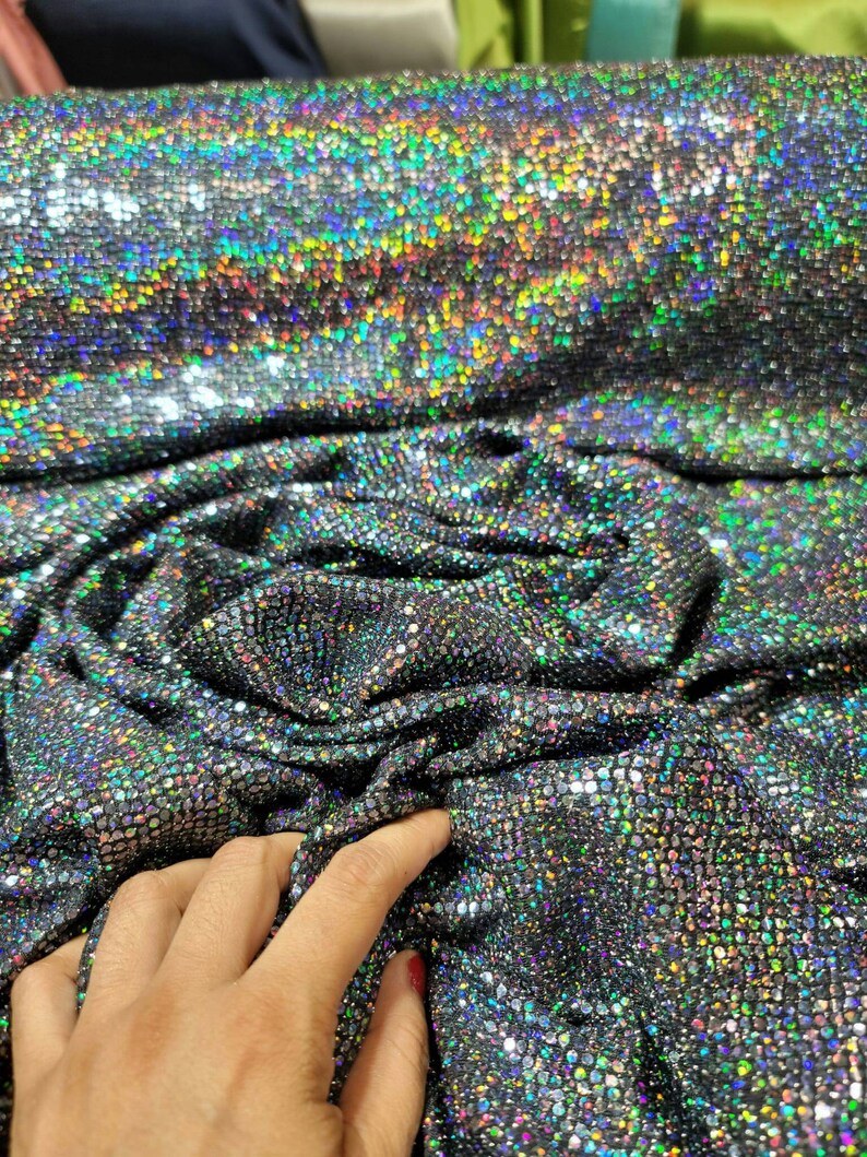 May include: Close-up of iridescent black fabric with a textured, sparkly finish. The fabric is folded and draped, showing its shimmery quality.