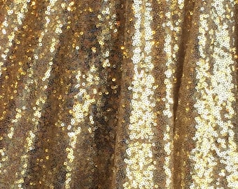 May include: Gold sequin fabric with a subtle shimmer. The sequins are tightly packed together, creating a smooth and luxurious texture.
