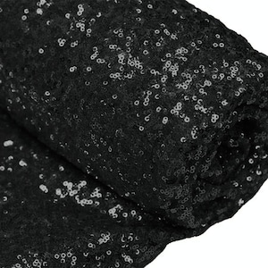 Könnte beinhalten: Schwarzer Paillettenstoff mit glänzender, glitzernder Oberfläche. Der Stoff ist aufgerollt und die Pailletten sind sichtbar.