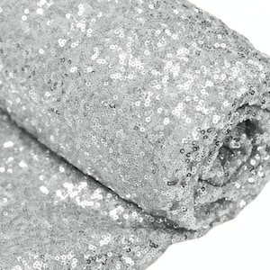 May include: Silver sequin fabric, a close-up of the sparkly material. The fabric is rolled up, showing the texture and shine of the sequins.