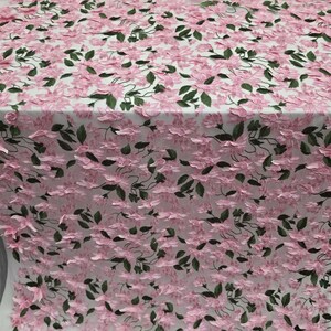 Puede incluir: Tela floral rosa con detalles de flores y hojas en 3D. La tela es de color rosa claro con hojas y tallos verdes oscuros. La tela est&aacute; enrollada en el fondo.