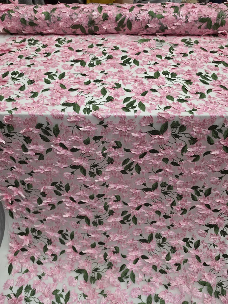 Puede incluir: Tela floral rosa con detalles de flores y hojas en 3D. La tela es de color rosa claro con hojas y tallos verdes oscuros. La tela est&aacute; enrollada en el fondo.