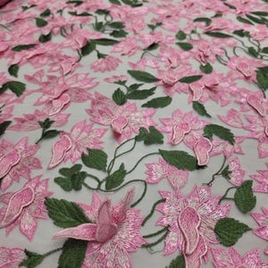 Puede incluir: Tela bordada con flores rosas y hojas verdes. La tela presenta un patr&oacute;n repetitivo de flores tridimensionales. Las flores son de un color rosa vibrante y las hojas de un verde intenso. La tela es adecuada para ropa o decoraci&oacute;n del hogar.