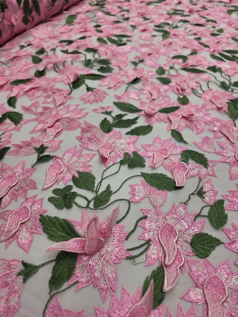 Puede incluir: Tela bordada con flores rosas y hojas verdes. La tela presenta un patr&oacute;n repetitivo de flores tridimensionales. Las flores son de un color rosa vibrante y las hojas de un verde intenso. La tela es adecuada para ropa o decoraci&oacute;n del hogar.