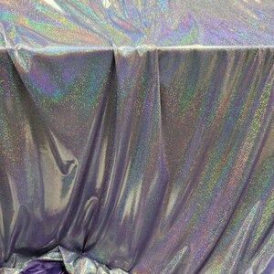 May include: A silver iridescent fabric with a subtle sparkle. The fabric is folded and draped over a purple surface.