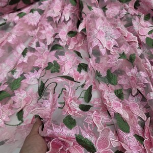 Puede incluir: Tela bordada con flores rosas con detalles de flores y hojas en 3D. La tela presenta una base transparente, con flores rosas y hojas verdes. Las flores est&aacute;n bordadas intrincadamente, creando un efecto texturizado y dimensional. Ideal para vestidos, faldas y otras prendas.