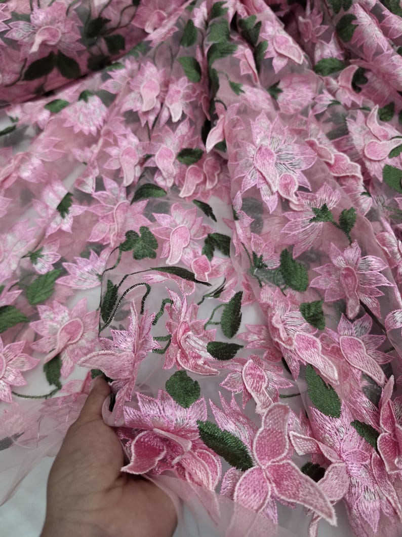 Puede incluir: Tela bordada con flores rosas con detalles de flores y hojas en 3D. La tela presenta una base transparente, con flores rosas y hojas verdes. Las flores est&aacute;n bordadas intrincadamente, creando un efecto texturizado y dimensional. Ideal para vestidos, faldas y otras prendas.