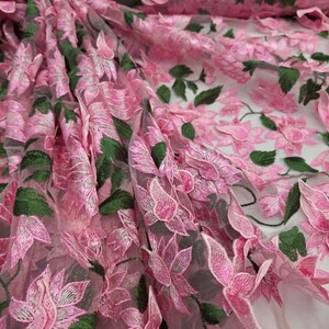 Puede incluir: Primer plano de tela bordada con flores rosas. La tela presenta flores rosas detalladas en tres dimensiones con hojas verdes, creando un efecto texturizado y en capas. El fondo transparente a&ntilde;ade profundidad al dise&ntilde;o. Ideal para proyectos de costura y manualidades.