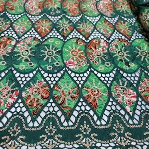 以下が含まれることがあります： 緑色のレース生地に花柄と金色のスパンコールが施されています。レースは波状の縁取りがされています。