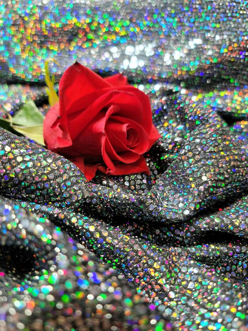 May include: A single red rose with green leaves rests on a silver sparkly fabric background.