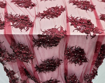May include: Burgundy floral lace fabric with a sheer mesh background and scattered rhinestones. The lace features a repeating pattern of large, three-dimensional flowers.