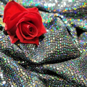 May include: A single red rose resting on a silver sequined fabric. The rose is in full bloom and has a delicate, velvety texture.