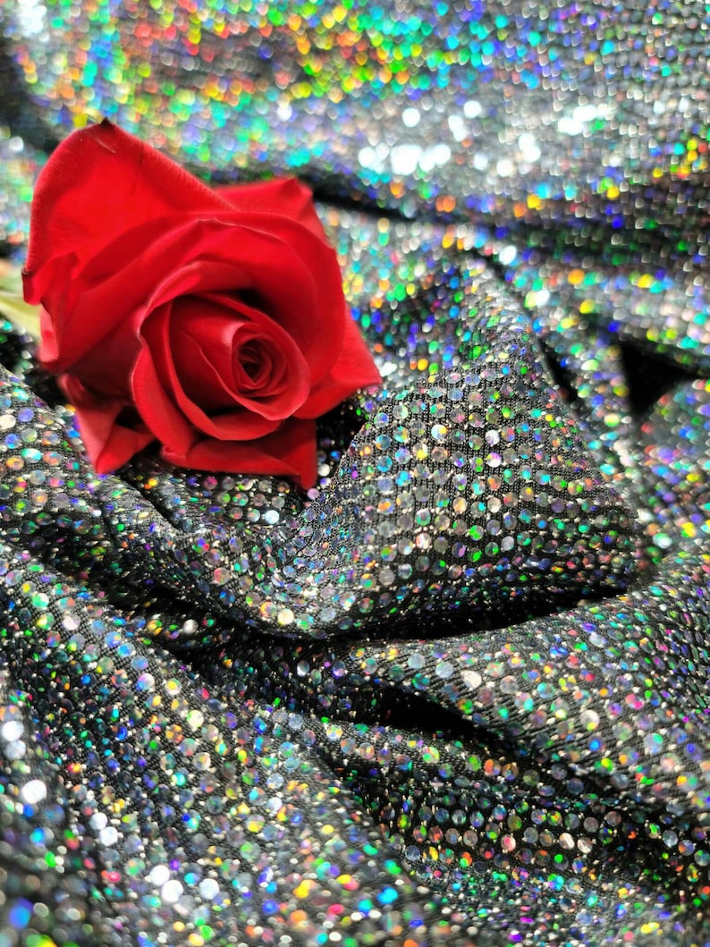 May include: A single red rose resting on a silver sequined fabric. The rose is in full bloom and has a delicate, velvety texture.