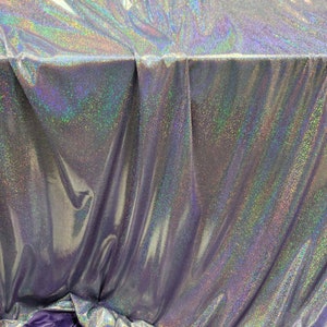 May include: A silver iridescent fabric with a subtle sparkle. The fabric is folded and draped over a purple surface.