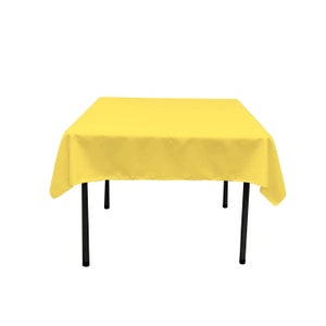 May include: A yellow square tablecloth with black metal legs. The tablecloth is made of a smooth, wrinkle-resistant fabric.