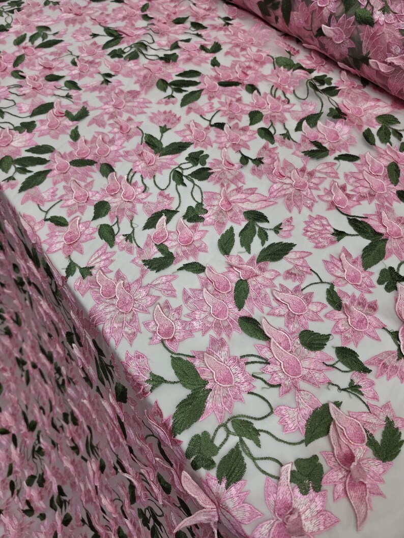 Puede incluir: Tela bordada con flores rosas y hojas y tallos verdes. La tela presenta un patr&oacute;n repetitivo de flores tridimensionales. Las flores son de color rosa suave y las hojas de color verde oscuro. Adecuado para ropa o decoraci&oacute;n del hogar.