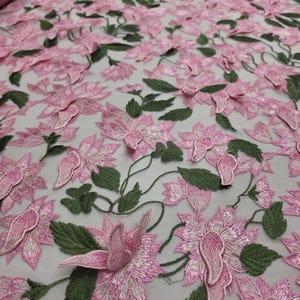 Puede incluir: Tela bordada con flores rosas y hojas verdes. La tela presenta un dise&ntilde;o tridimensional de flores rosas y hojas verdes, creando una apariencia texturizada y detallada. La tela se utiliza probablemente para ropa o decoraci&oacute;n del hogar.