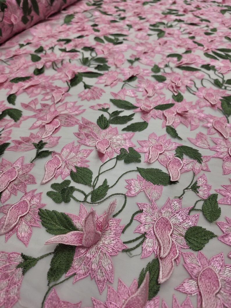 Puede incluir: Tela bordada con flores rosas y hojas verdes. La tela presenta un dise&ntilde;o tridimensional de flores rosas y hojas verdes, creando una apariencia texturizada y detallada. La tela se utiliza probablemente para ropa o decoraci&oacute;n del hogar.