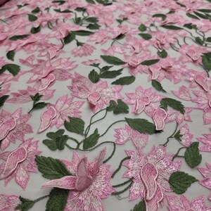 Puede incluir: Tela bordada con flores rosas y hojas verdes. La tela presenta un dise&ntilde;o tridimensional de flores rosas y hojas verdes, creando una apariencia texturizada y detallada. La tela se utiliza probablemente para prendas de vestir o fines decorativos.