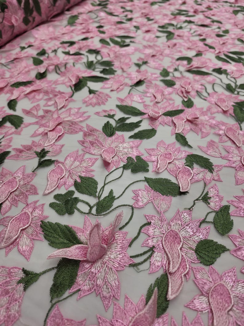 Puede incluir: Tela bordada con flores rosas y hojas verdes. La tela presenta un dise&ntilde;o tridimensional de flores rosas y hojas verdes, creando una apariencia texturizada y detallada. La tela se utiliza probablemente para prendas de vestir o fines decorativos.